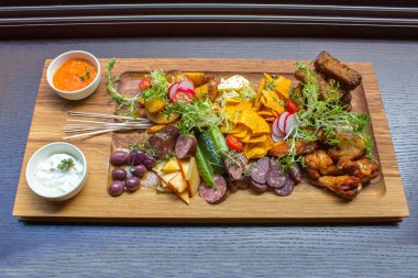 Ürün yelpazesine aperatifler eti, tavuk budu, sarımsak ekmek, sebze, turuncu ve siyah beyaz soslar üzerinde kahverengi ahşap tabakta tablo arka plan