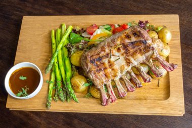 Lezzetli kuzu eti crown kızartma sebze salatası ve kahverengi ahşap masa ahşap tepside üzerinde kahverengi sos ile