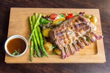 Lezzetli kuzu eti crown kızartma sebze salatası ve kahverengi ahşap masa ahşap tepside üzerinde kahverengi sos ile