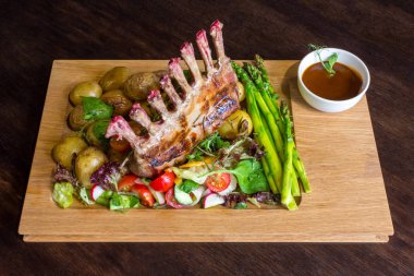 Lezzetli kuzu eti crown kızartma sebze salatası ve kahverengi ahşap masa ahşap tepside üzerinde kahverengi sos ile