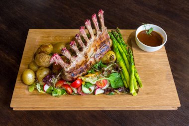 Lezzetli kuzu eti crown kızartma sebze salatası ve kahverengi ahşap masa ahşap tepside üzerinde kahverengi sos ile