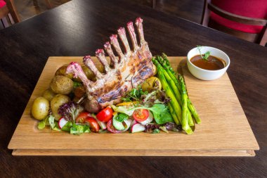 Lezzetli kuzu eti crown kızartma sebze salatası ve kahverengi ahşap masa ahşap tepside üzerinde kahverengi sos ile