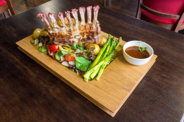 Lezzetli kuzu eti crown kızartma sebze salatası ve kahverengi ahşap masa ahşap tepside üzerinde kahverengi sos ile