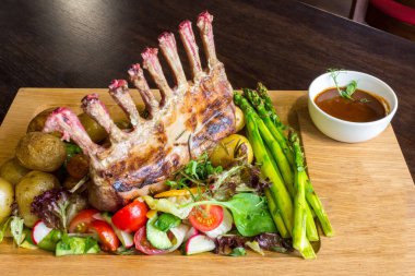 Lezzetli kuzu eti crown kızartma sebze salatası ve kahverengi ahşap masa ahşap tepside üzerinde kahverengi sos ile