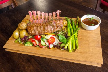 Lezzetli kuzu eti crown kızartma sebze salatası ve kahverengi ahşap masa ahşap tepside üzerinde kahverengi sos ile