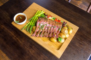 Lezzetli kuzu eti crown kızartma sebze salatası ve kahverengi ahşap masa ahşap tepside üzerinde kahverengi sos ile