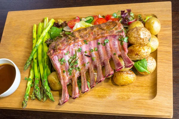 Lezzetli kuzu eti crown kızartma sebze salatası ve kahverengi ahşap masa ahşap tepside üzerinde kahverengi sos ile