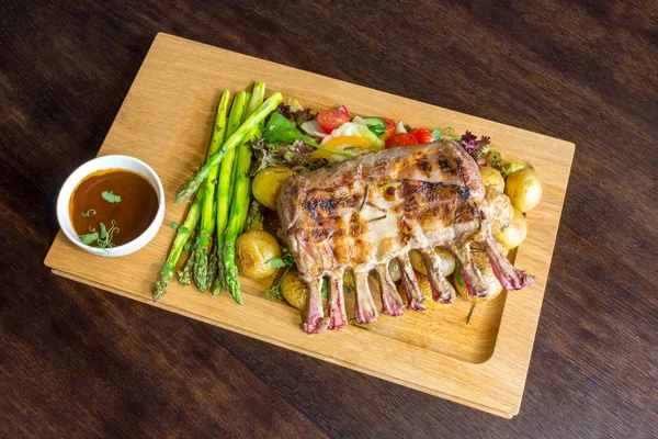 Lezzetli kuzu eti crown kızartma sebze salatası ve kahverengi ahşap masa ahşap tepside üzerinde kahverengi sos ile