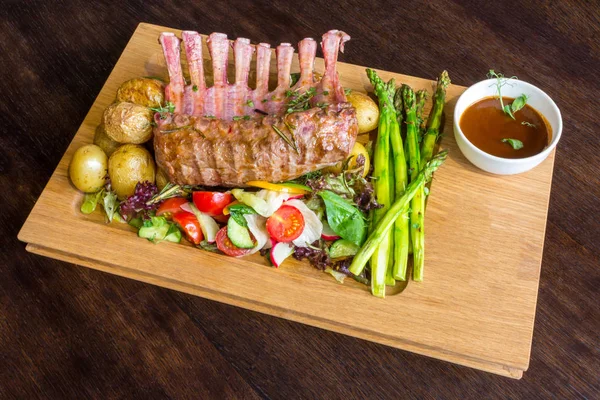 Lezzetli kuzu eti crown kızartma sebze salatası ve kahverengi ahşap masa ahşap tepside üzerinde kahverengi sos ile