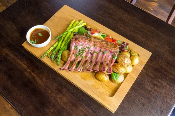 Lezzetli kuzu eti crown kızartma sebze salatası ve kahverengi ahşap masa ahşap tepside üzerinde kahverengi sos ile