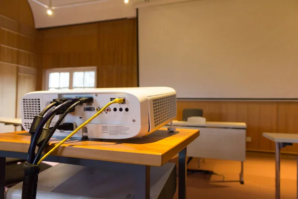 White screen projector in front of a screen in a conference or lecture hall with a white projector screen