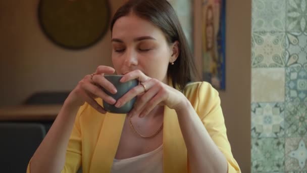 Una chica bebe delicioso café en una cafetería. El camarero trae un café feliz chica hermosa. Una mujer se sienta sola en una cafetería — Vídeo de stock