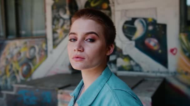 Portrait d'une jeune fille indépendante moderne contre un mur avec des graffitis. Femme aux cheveux courts, gros plan . Séquence Vidéo