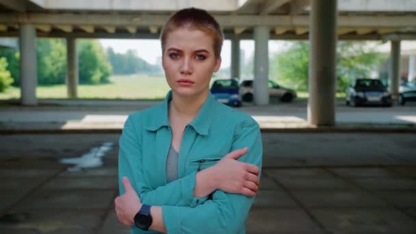 Молодая сильная женщина стоит одна на парковке, портрет девушки с короткими волосами и курткой — стоковое видео