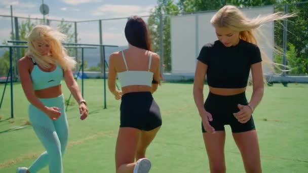 Drie meisjes doen hurken in het park, twee blondjes en een brunette van atletische bouw doen fitness oefeningen in de frisse lucht . — Stockvideo