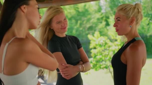 Vrouwen in sportkleding praten met elkaar, een gelukkig blondje luistert naar de coach, twee meisjes en één vrouw communiceren en glimlachen. — Stockvideo