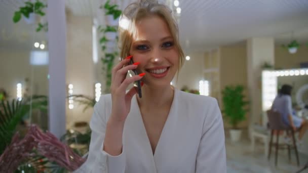 En kvinna pratar i telefon i en skönhetssalong, en flicka efter procedurer i studion, en glad blondin ler — Stockvideo