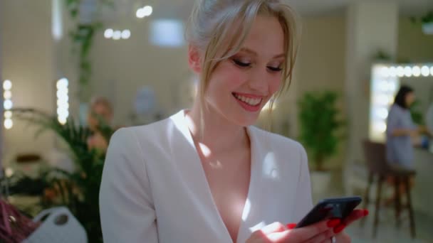 Egy lány begépel egy üzenetet a telefonjába, egy fiatal, elegáns szőke ír egy üzenetet, egy boldog nő mosolyog. — Stock videók