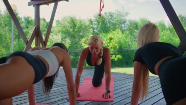 Un entrenador feliz conduce una clase al aire libre, una mujer muestra el ejercicio en sus pies con el ejemplo, dos niñas repiten. — Vídeos de Stock