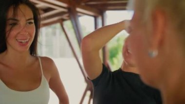 Spor giyinen kadınlar birbirleriyle konuşur, diş teli takan mutlu bir esmer bir antrenör, iki kız ve bir kadın sohbet eder ve gülümser..