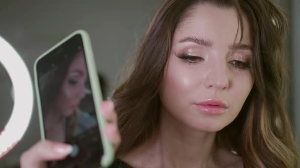 메이크업 아티스트가 현대 전화의 렌즈 아래있는 아름다운 모델의 테스트 샷을 사용하는 모습 — 비디오