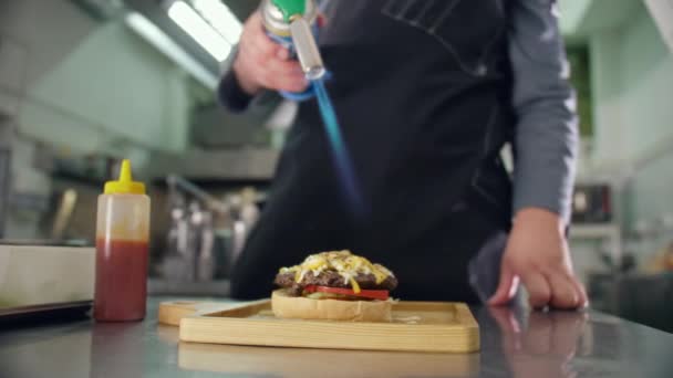 Kochen eines Cheeseburgers, der Cook Stokes Parmesan und Cheddar mit einem Gasbrenner, moderne Kochen eines Cheeseburgers, die Flamme des Feuers schmilzt den zarten Käse — Stockvideo