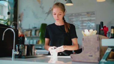 Barista tek kullanımlık bir bardağın kapağını kapatıp bize veriyor. Kahve dükkanında çalışan gülümseyen kız. .