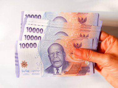 Woman hand holding stack of Indonesian money currency banknotes ten thousand rupiah isolated on white background. Cash payment concept.