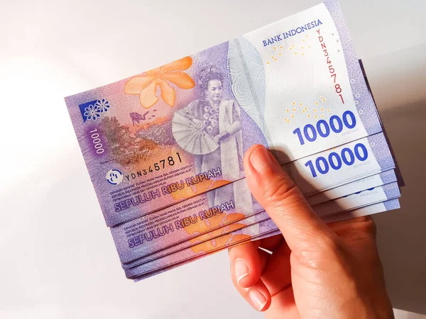 Woman hand holding stack of Indonesian money currency banknotes ten thousand rupiah isolated on white background. Cash payment concept.