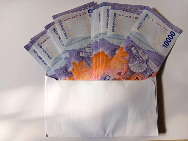 Stack of Indonesian money currency banknotes ten thousand rupiah inside a white envelope isolated on white background. Copy space for text.