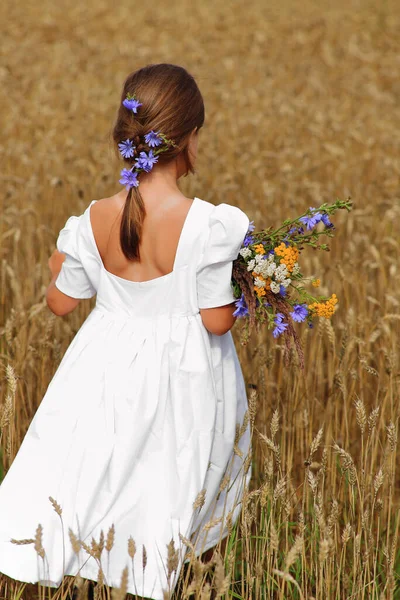 Little girl with a bouquet of wildflowers in her hands in a wheat field. — Stock Photo, Image