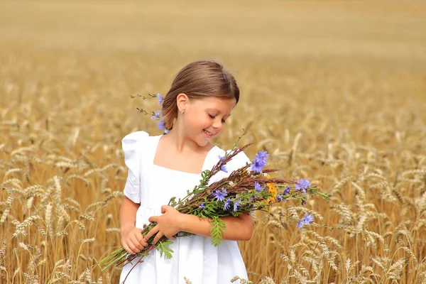 Petite fille avec un bouquet de fleurs sauvages dans ses mains dans un champ de blé. — Photo