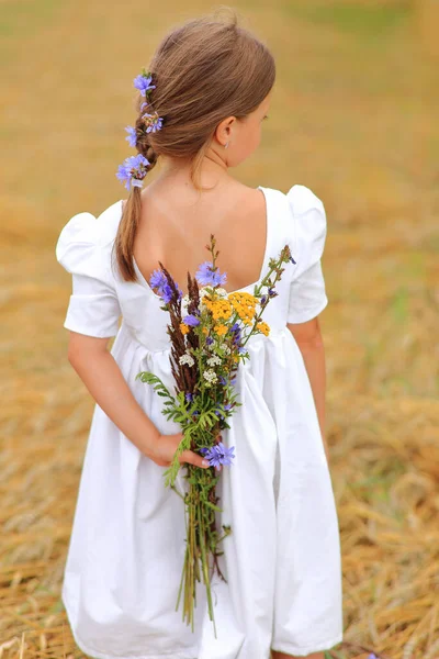 Menina com um buquê de flores silvestres em suas mãos em um campo de trigo . — Fotografia de Stock