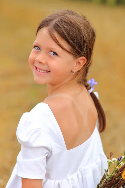 Маленькая девочка с букетом полевых цветов в руках на пшеничном поле. — стоковое фото