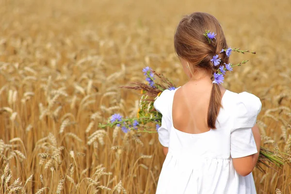 Kleines Mädchen mit einem Strauß Wildblumen in der Hand in einem Weizenfeld. — Stockfoto