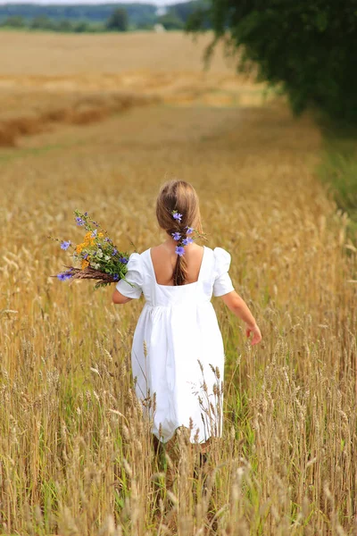 Mała dziewczynka z bukietem dzikich kwiatów w rękach na polu pszenicy. — Zdjęcie stockowe