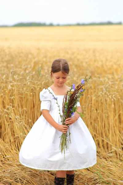 Petite fille avec un bouquet de fleurs sauvages dans ses mains dans un champ de blé. — Photo