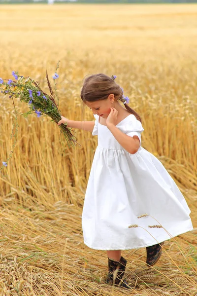 Menina com um buquê de flores silvestres em suas mãos em um campo de trigo . — Fotografia de Stock