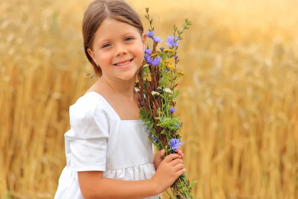 Menina com um buquê de flores silvestres em suas mãos em um campo de trigo . — Fotografia de Stock