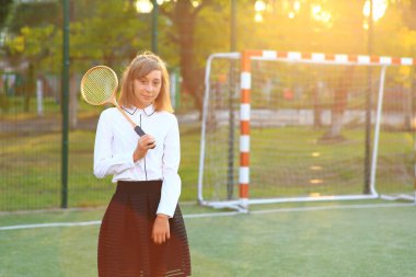 Futbol sahasında elinde raketle okul üniformalı bir kız..