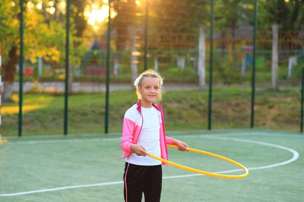 Fille dans un survêtement avec un cerceau dans ses mains sur le terrain de jeu — Photo