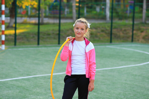Девушка в спортивном костюме с обручем в руках на детской площадке