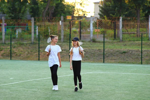 Dwie dziewczyny po lekcjach idą na tenisa na plac zabaw.. — Zdjęcie stockowe