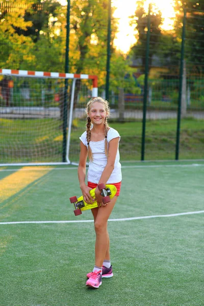 Девушка со скейтбордом в руках на детской площадке — стоковое фото