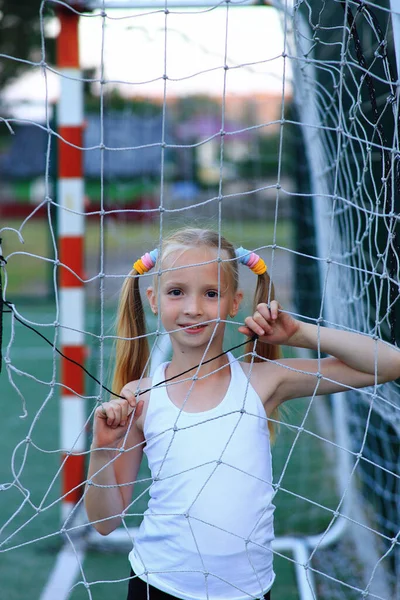 En flicka som poserar nära ett fotbollsmål på en idrottsplan. — Stockfoto