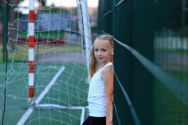 Egy lány pózol egy focipálya mellett egy sportpályán.. — Stock Fotó