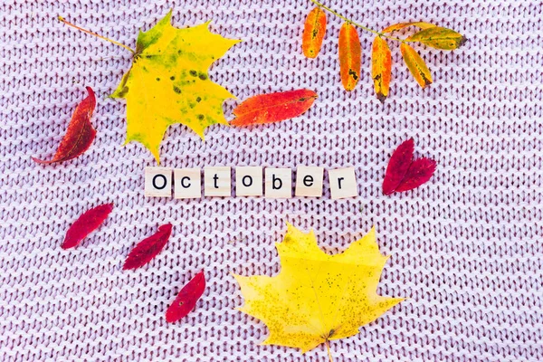 Ένα κίτρινο φύλλο και οι λέξεις Οκτώβριος βρίσκονται σε πλεκτό φόντο. — Φωτογραφία Αρχείου