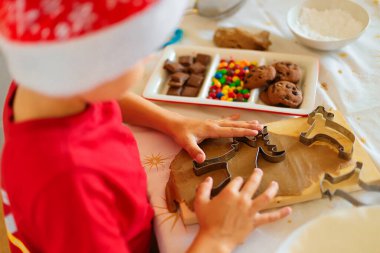 Noel Baba şapkalı bir çocuk mutfakta kurabiye hazırlıyor..