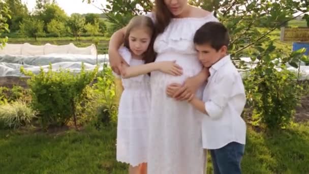 Uma mãe grávida com dois filhos está andando no jardim perto da casa. — Vídeo de Stock