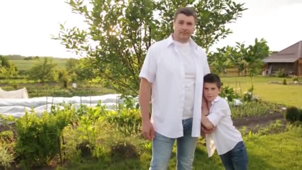 Pai e filho caminham juntos no jardim verde perto da casa. — Vídeo de Stock